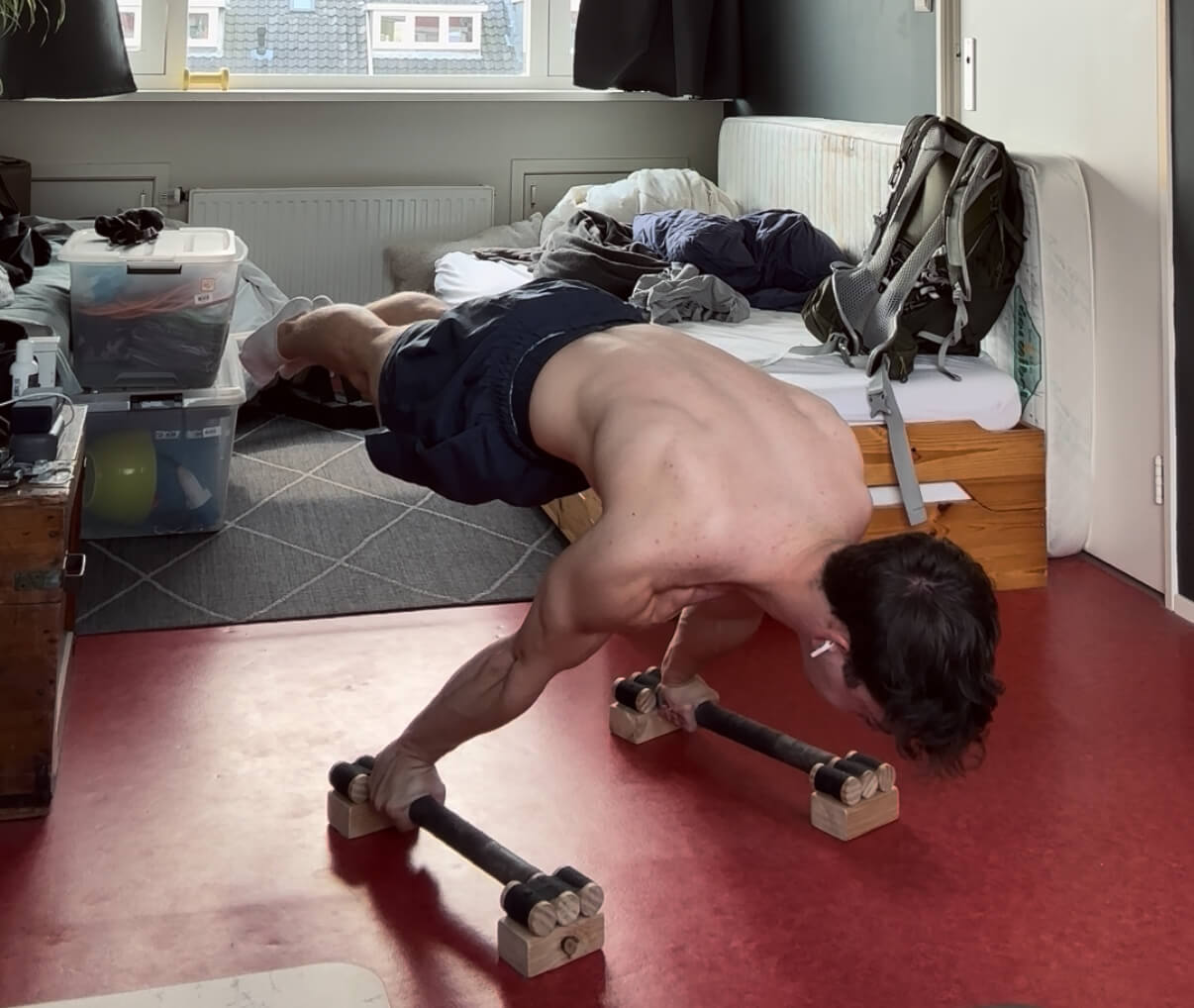 Holding a planche, a power move where you hold your body horizontal on the ground by leaning forward on your shoulders while your feet are off the ground. The background is a messy room.