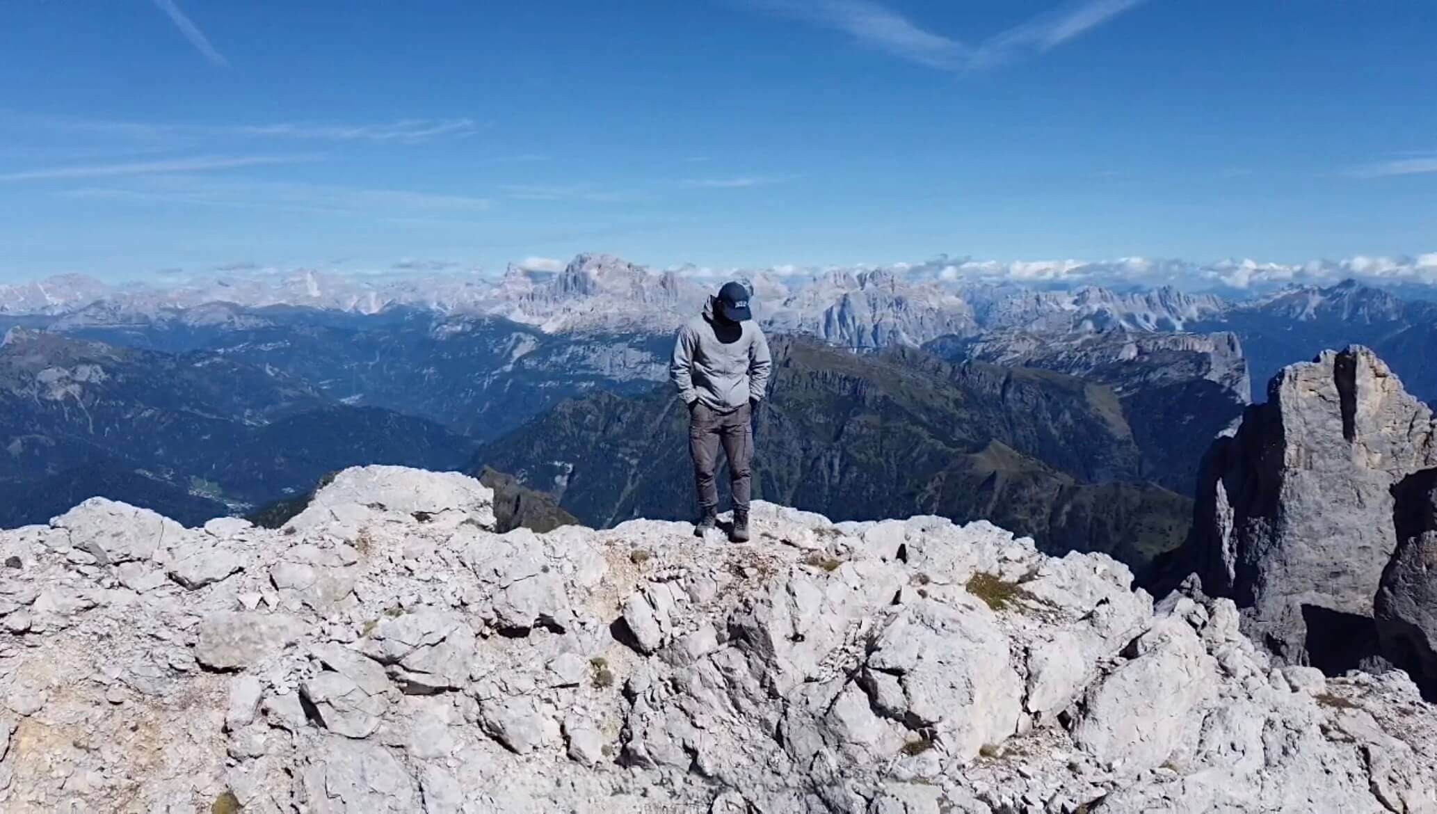 Me standing on a mountain with a lot of mountains far in the background. The sky is blue with some clouds.